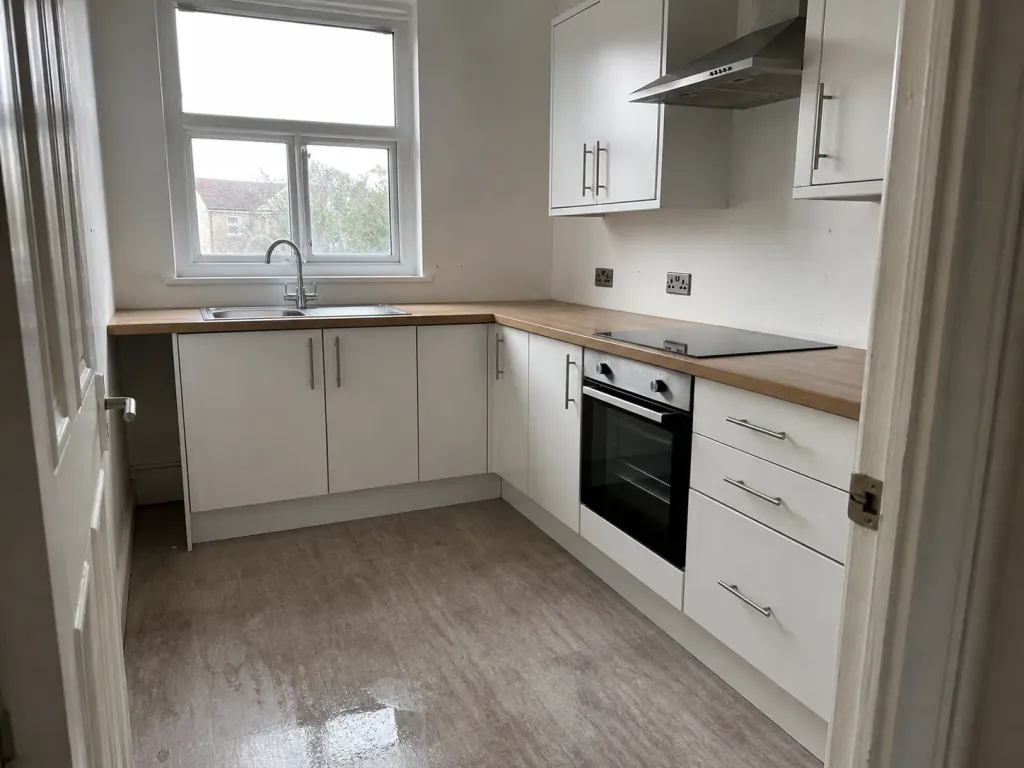 A just-cleaned empty kitchen, worktops bare and the floor still drying near the sink