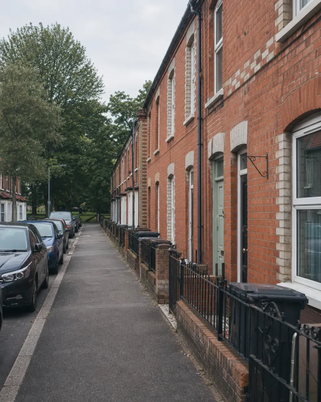 Two-storey Victorian terraces close to the pavement on a Newtown street, pale brick arches over the doors and park trees at the far end
