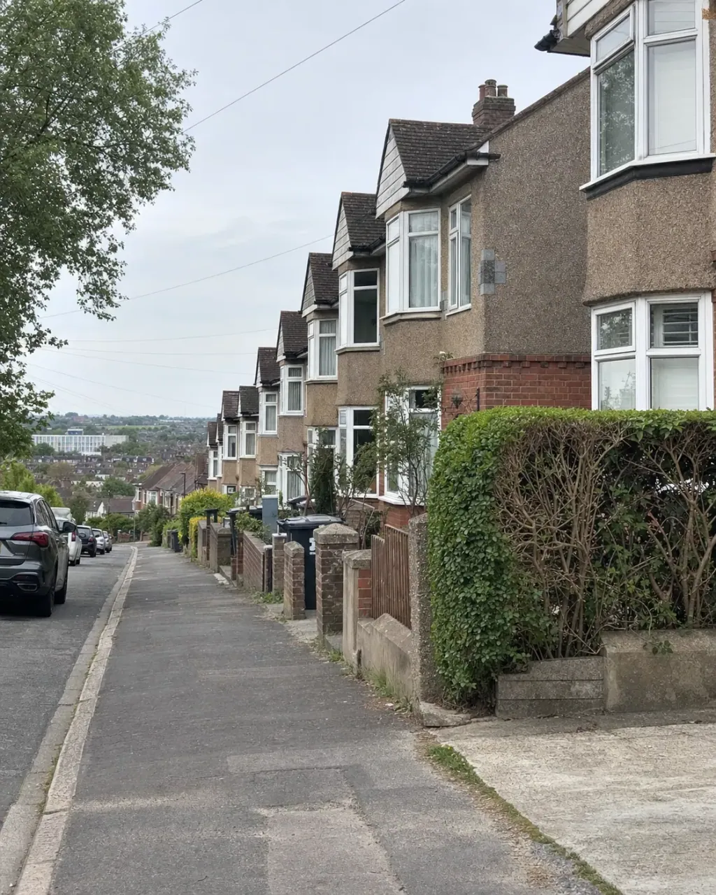 Bay-fronted 1930s semis with pebbledash upper storeys stepping down a Norcot street, rooftops of Reading in the valley below