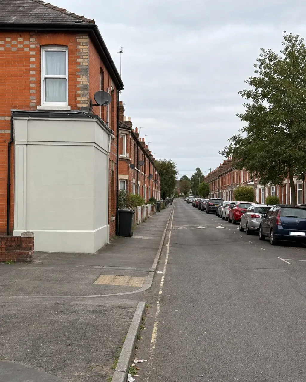 A long straight terraced street in West Reading, satellite dishes at first floor level and cars parked nose to tail along the kerb