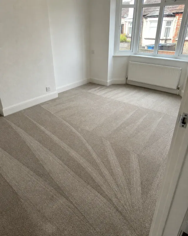 An empty living room after an end of tenancy clean, fresh hoover lines in the carpet, bare bay window and radiator