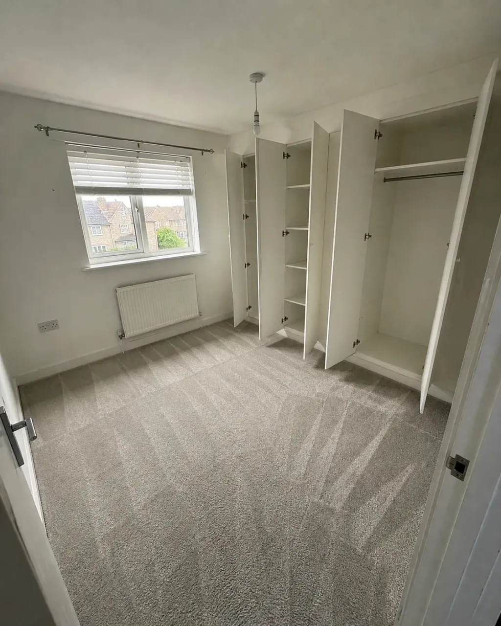 An empty bedroom with fitted wardrobes open on bare shelves and rails after checkout