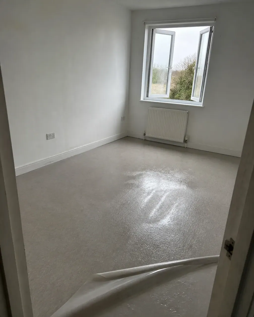 A bare room after disinfection, vinyl floor still glistening and protective film part rolled back at the door