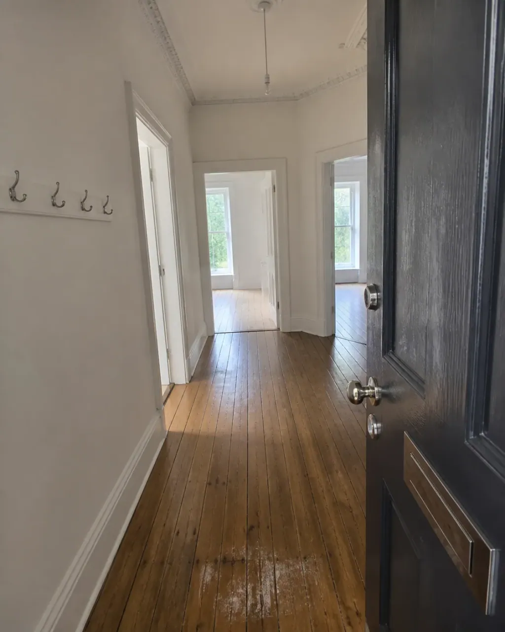 A restored hallway with fresh white walls and ceiling, floorboards cleaned back to the front door