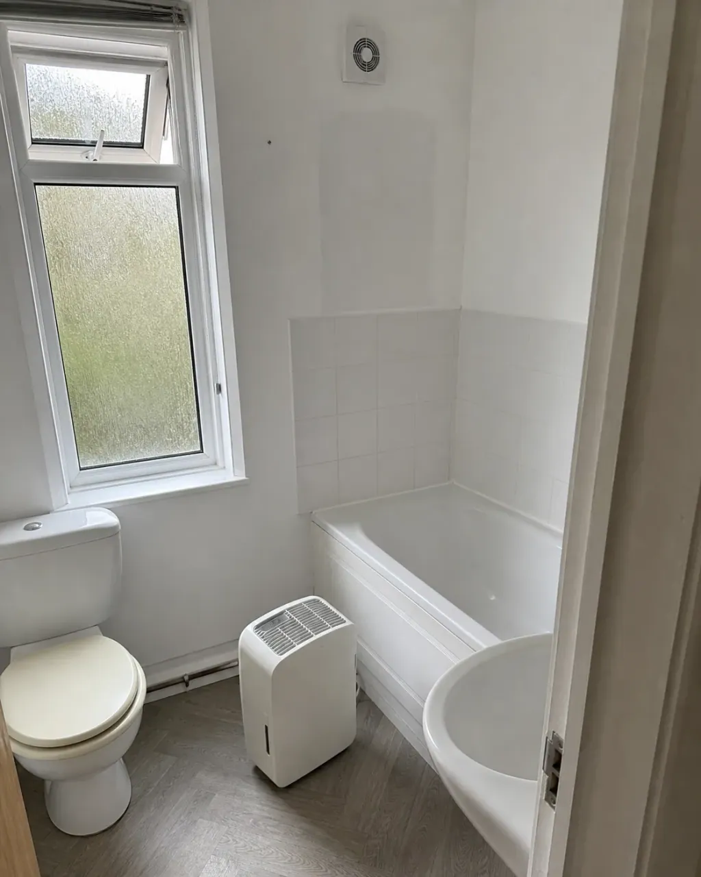 A small bathroom after mould remediation, window opened and a dehumidifier standing on the floor