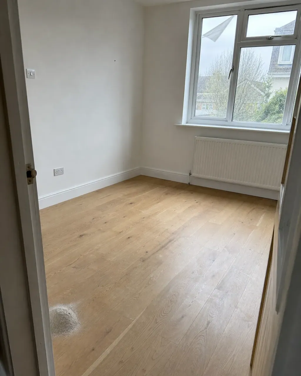 A renovated room with new flooring, a small pile of plaster dust swept up and window film part peeled